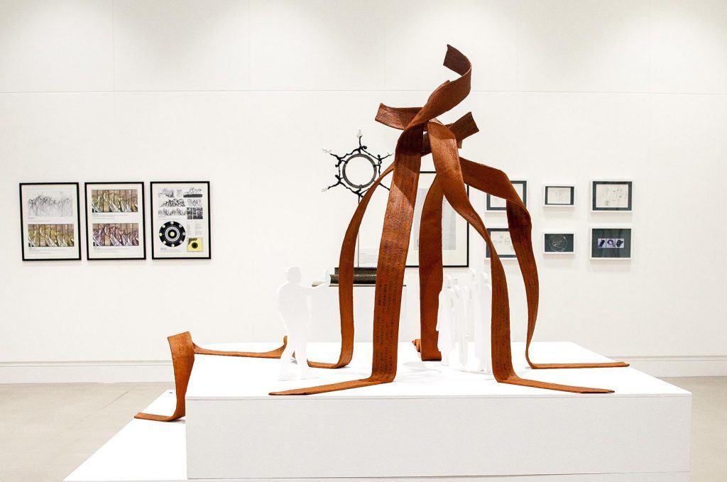 A scaled model of the proposed artwork, formed of rigid copper-coloured flowing ribbons twisting and reaching up to a point, presented in a gallery space 