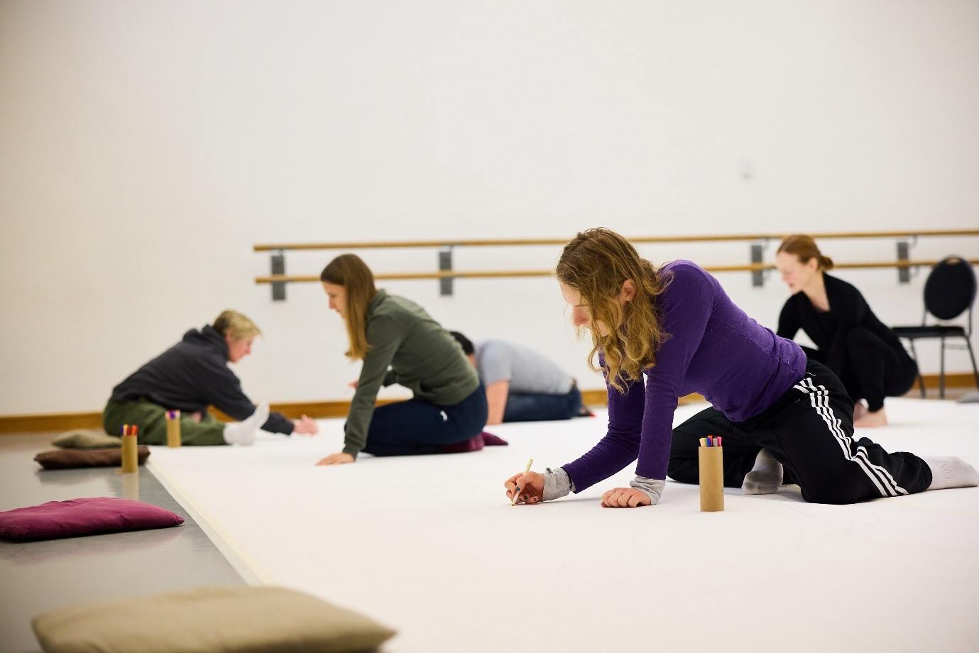 People sit on the floor drawing on a large white sheet of paper