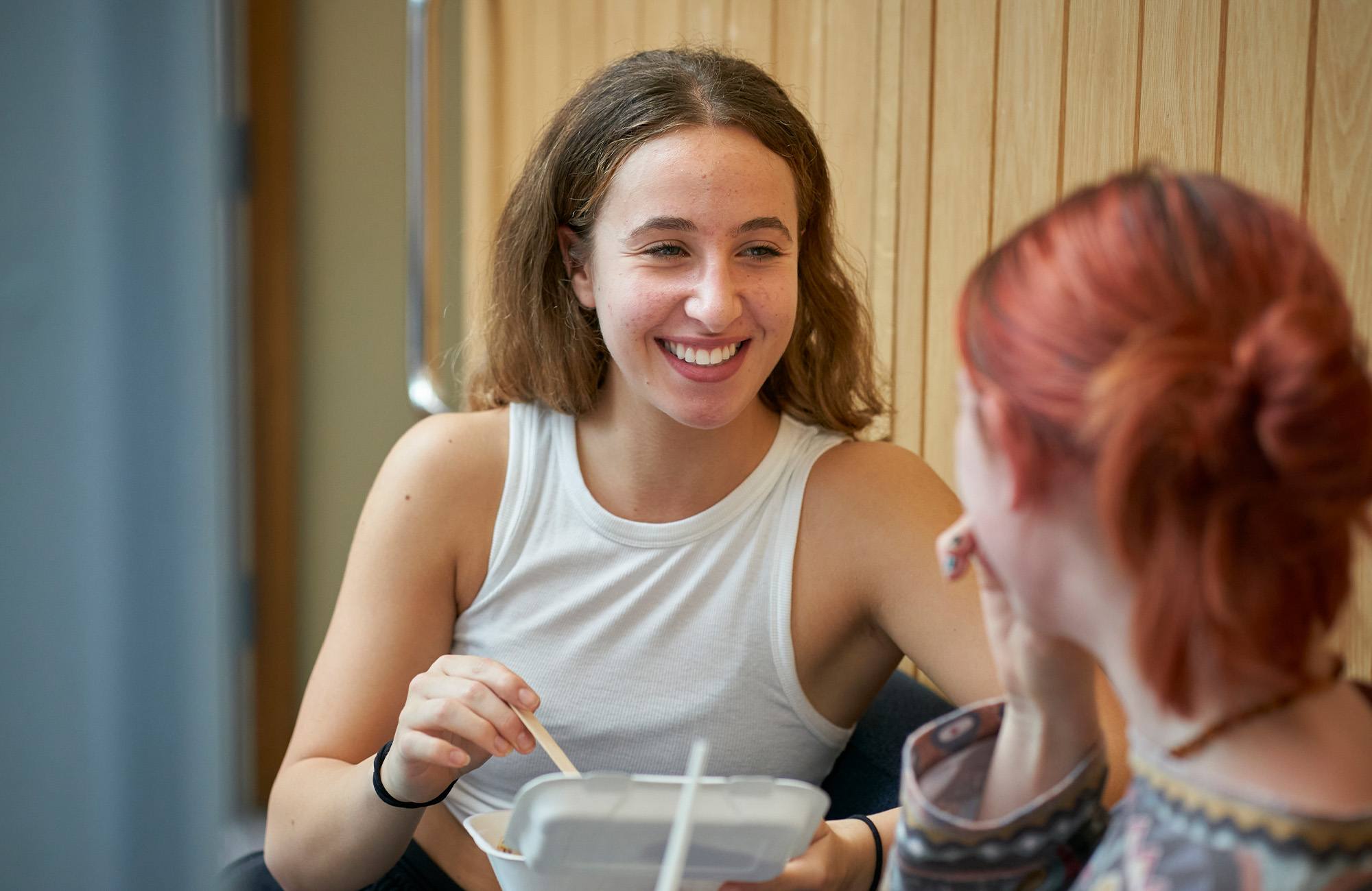 Two students sat in the canteen eating and smiling